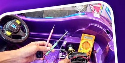 Technician testing wiring inside a kids battery car dashboard